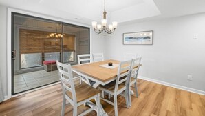 A dining area with a wooden table and white chairs, a chandelier, and a sliding glass door leading to an outdoor space. - 3BR Golf Villa Near Beach & Fairway Views (Pawleys Island)