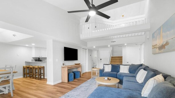A spacious living area with a blue sofa, a coffee table, and a dining set. A TV is mounted on the wall, and there is a staircase leading to an upper level. - 3BR Golf Villa Near Beach & Fairway Views (Pawleys Island)