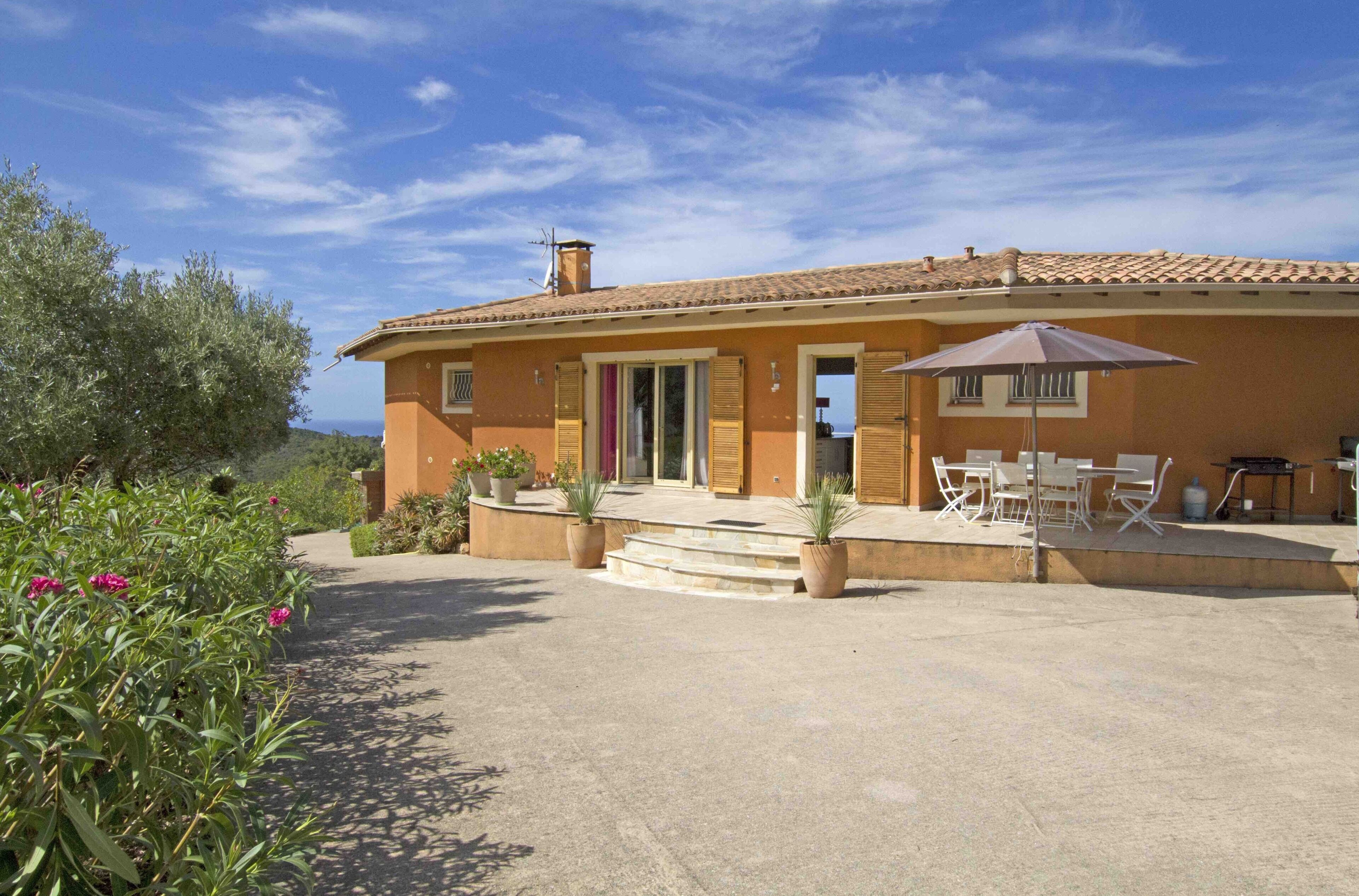 A Mediterranean-style house with a tiled roof, a covered patio with outdoor furniture, and a view of the sea.