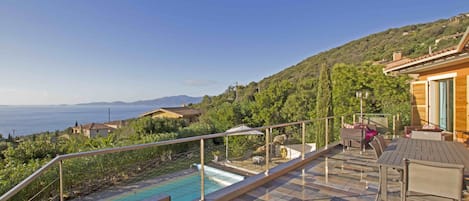 A rooftop pool area with a view of the sea, outdoor furniture, and a stone-tiled deck.