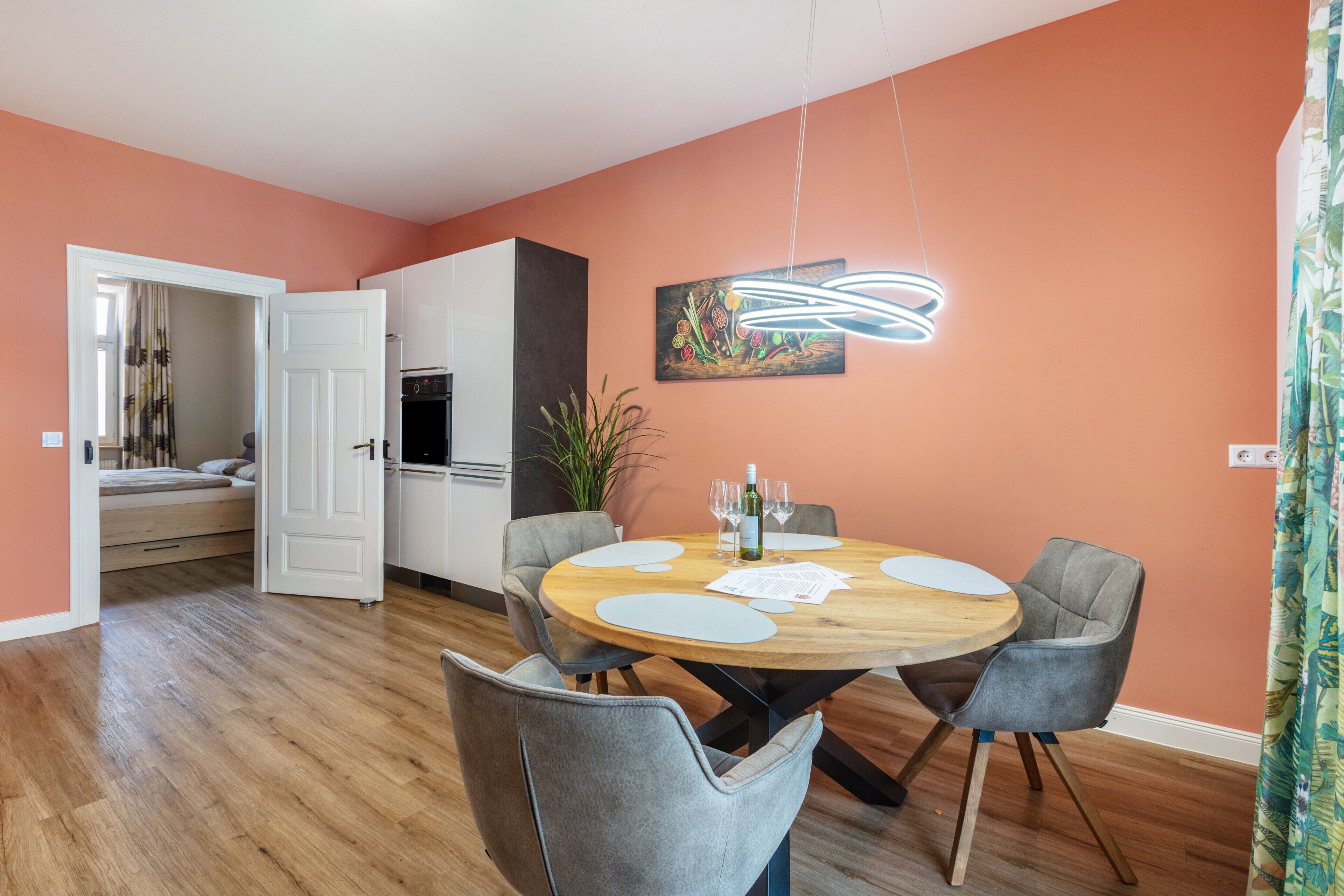 A dining area with a round wooden table, grey upholstered chairs, and a modern pendant light.