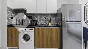 Una cucina compatta con lavatrice, frigorifero e zoccolo piastrellato.