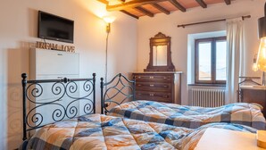Een slaapkamer met een bed, een dressoir, een spiegel, een televisie en een raam met gordijnen.