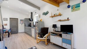 Una sala de estar moderna con techo de madera, zona de comedor, cocina y televisor sobre un mueble de madera.