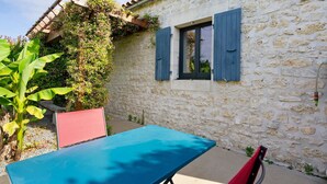 Un edificio de piedra con ventana y contraventanas, una mesa y una silla.