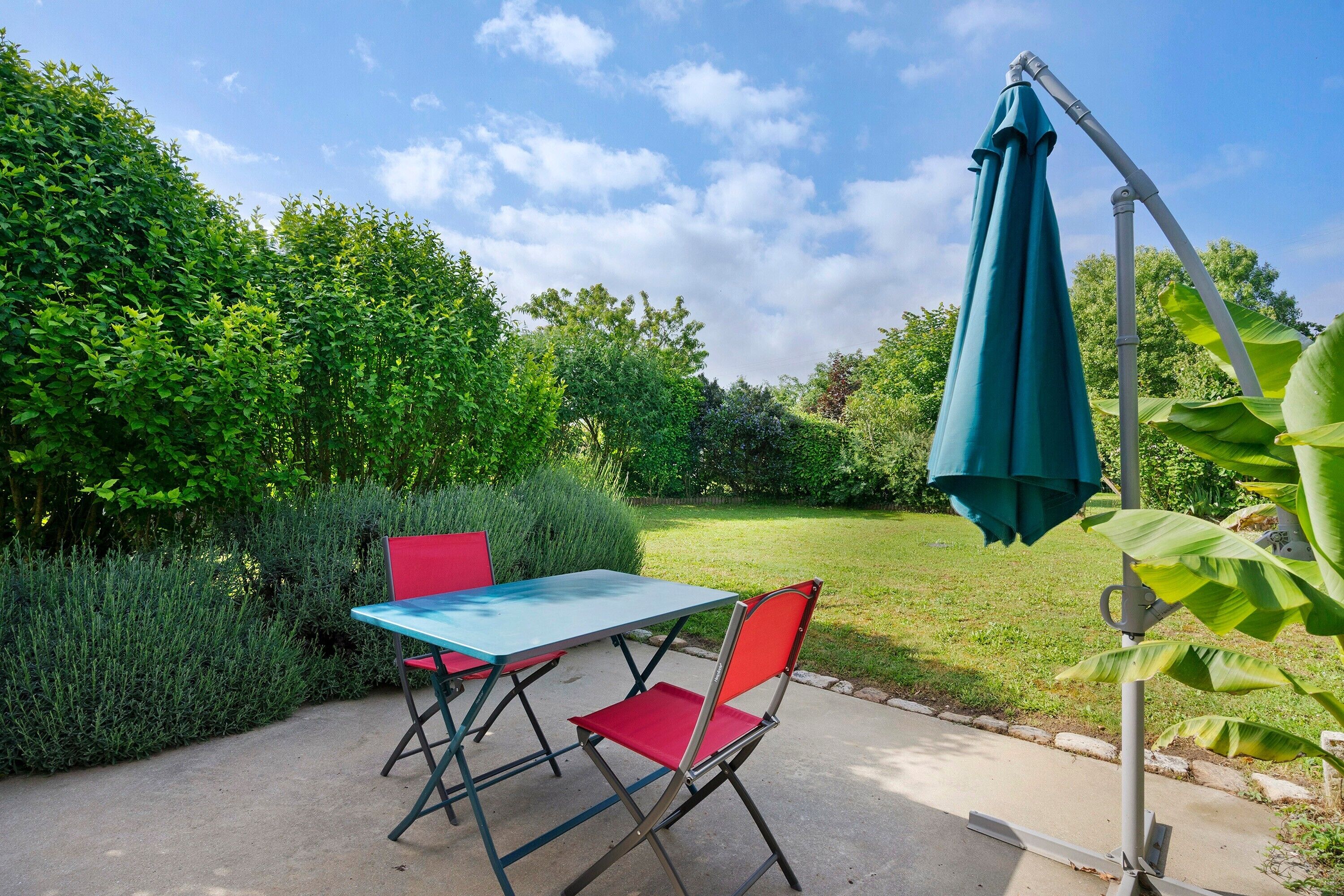 Une terrasse avec une table et des chaises, un parasol et une vue sur le jardin.