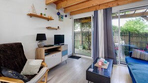 Una sala de estar con sofá, televisor, estanterías de madera y una puerta corrediza de vidrio hacia el exterior.