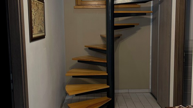A modern spiral staircase with wooden steps and black railings, leading to an upper floor. - Gîte de l'Api de Broque (Fréland)