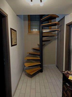 A modern spiral staircase with wooden steps and black railings, leading to an upper floor. - Gîte de l'Api de Broque (Fréland)
