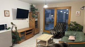 A living room with a flat-screen TV, wooden entertainment unit, green sofa, and a small coffee table. - Gîte de l'Api de Broque (Fréland)