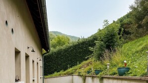 A narrow outdoor corridor with a concrete wall on one side and a building on the other. There are planters and outdoor lighting fixtures along the wall. - Gîte de l'Api de Broque (Fréland)