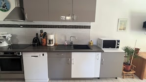 A modern kitchen with grey cabinets, a black countertop, a microwave, a coffee maker, and a dishwasher. - Gîte de l'Api de Broque (Fréland)