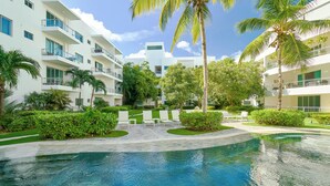A modern hotel with a swimming pool, palm trees, and a well-maintained garden.