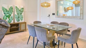 A dining area with a glass table, six chairs, and hanging pendant lights.