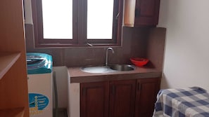 Une petite cuisine avec une fenêtre, un évier et un saladier rouge posé sur le plan de travail.