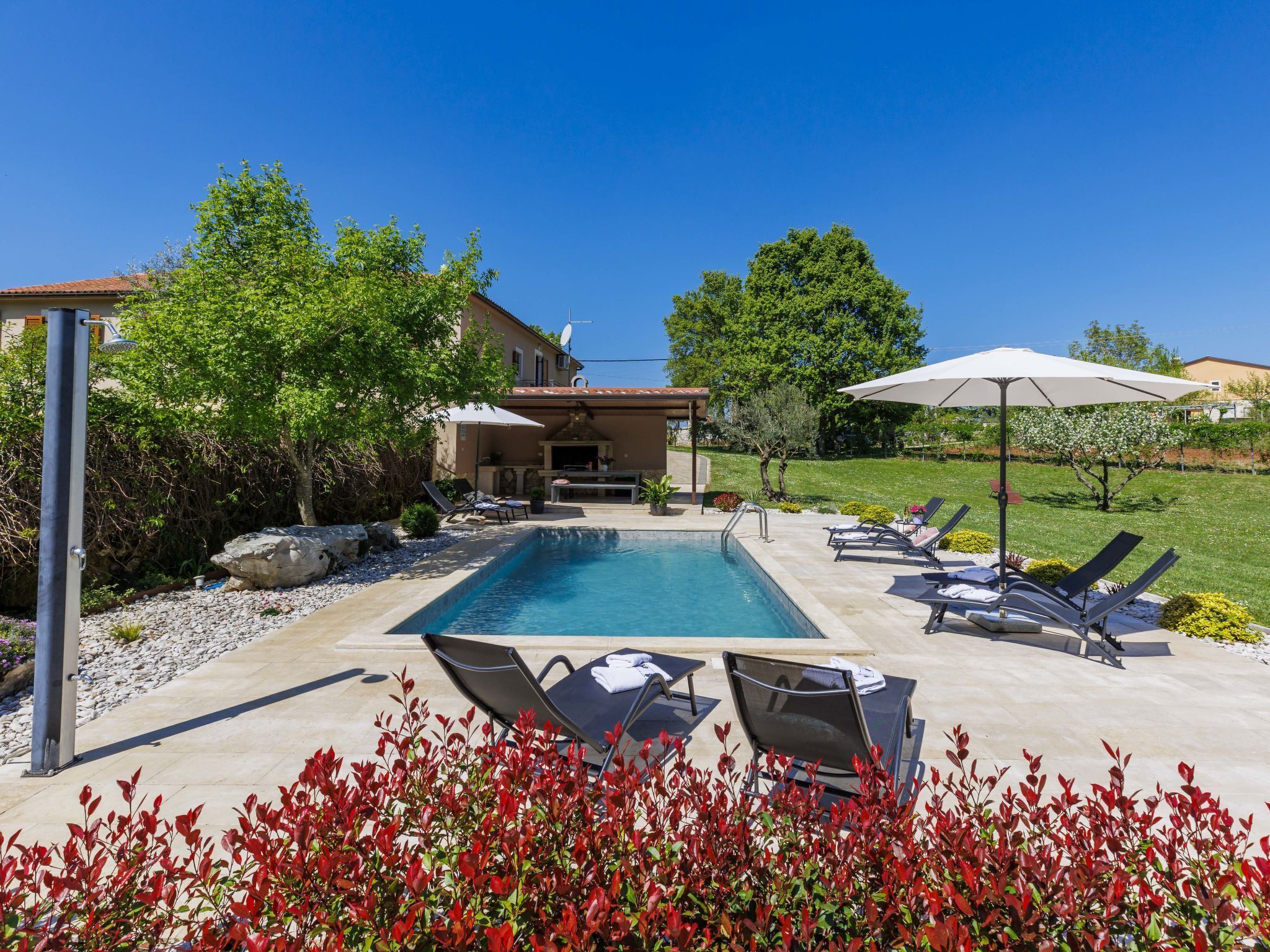 A swimming pool with lounge chairs, a barbecue area, and a patio with a pergola.