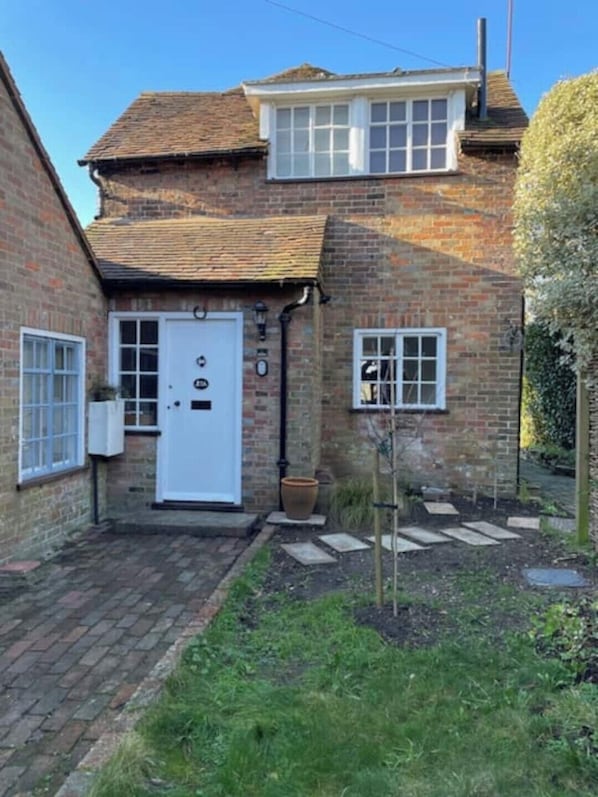 A brick house with a white door, two windows, and a small garden area with stepping stones.