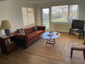 A living room with a brown sofa, a coffee table, a lamp, a TV, and a bookshelf.