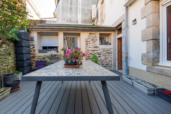 A wooden deck with a table, potted plants, and a stone wall.