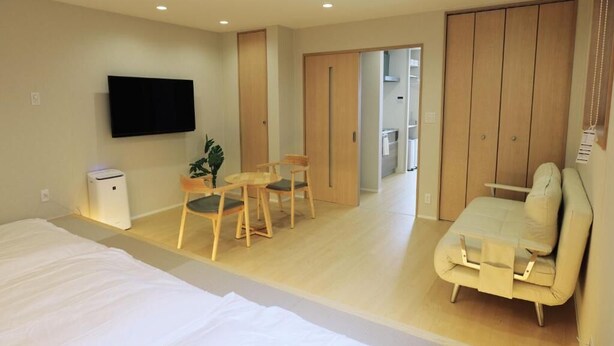 Habitación de hotel con cama, televisor, escritorio con sillas, sofá y armario.