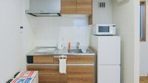 Cocina compacta con microondas, tetera y lavabo. Cuenta con alacenas de madera y encimera blanca.