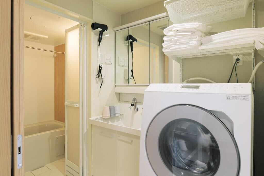 A compact bathroom with a washing machine, a towel rack, and a mirror.