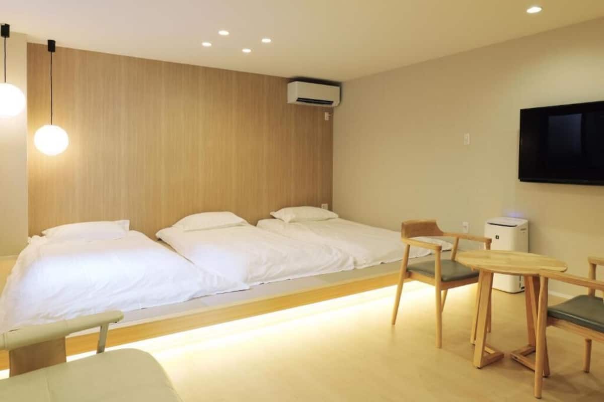 A hotel room with two beds, a desk, a chair, and a TV.