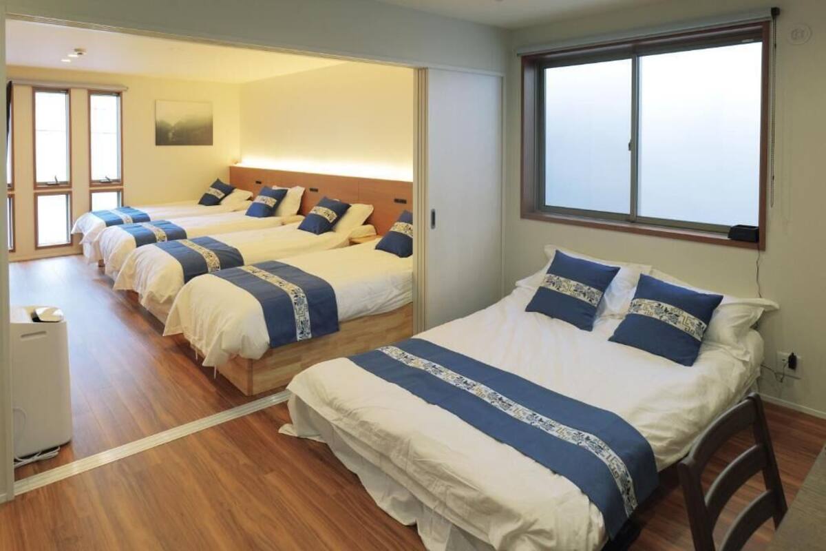 A hotel room with three beds arranged in a row, a large window, and a sliding door leading to another room.