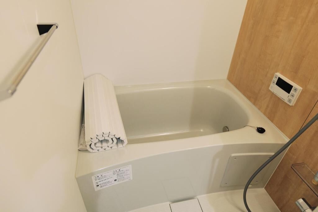 A small, white bathtub with a control panel on the wall, a towel on the edge, and a wooden panel on the right.