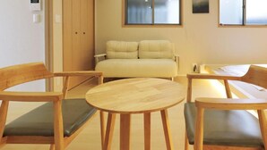 Una habitación con una cama, dos sillas de madera con cojines, una mesita redonda y una ventana.