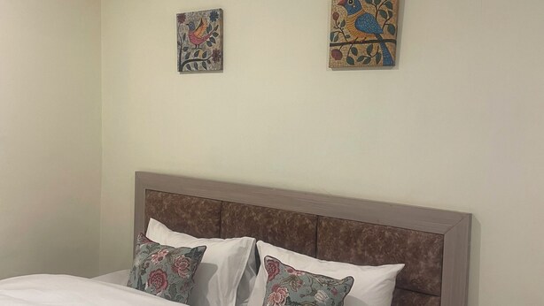 Una cama bien hecha con sábanas blancas y almohadas estampadas con motivos florales, un cabecero de madera y dos obras de arte colgadas en la pared que representan aves.