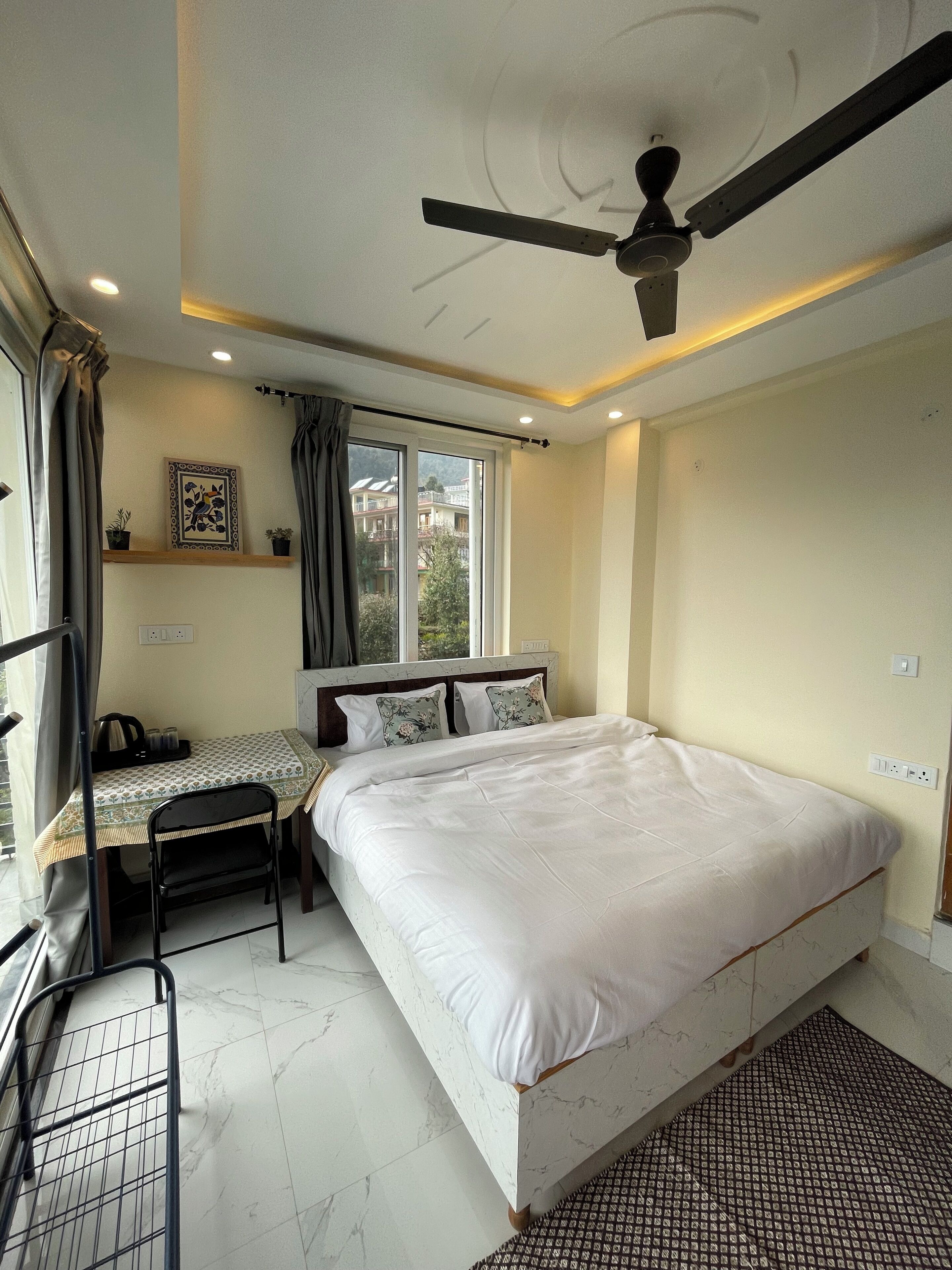 Un dormitorio con cama, escritorio, silla, ventilador de techo y ventana con cortinas.