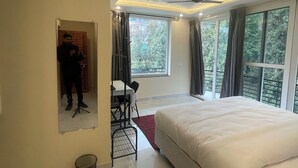 Ein modernes Schlafzimmer mit einem großen Bett, einem Schreibtisch mit Stuhl, einem Deckenventilator und großen Fenstern mit Vorhängen.