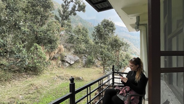 Ein Balkon mit Blick auf eine Berglandschaft, einem Holgitter und einer sitzenden Person.