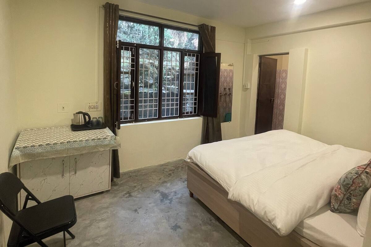 Een slaapkamer met een bed, een bureau met stoel, een raam met gordijnen en een deur.
