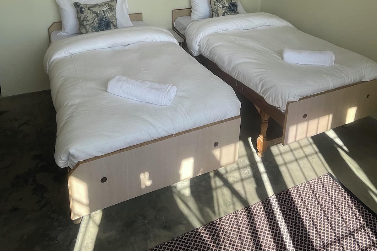 Een kamer met twee eenpersoonsbedden, elk met een houten frame en witte beddengoed. Boven de bedden hangt een klein decoratief object.