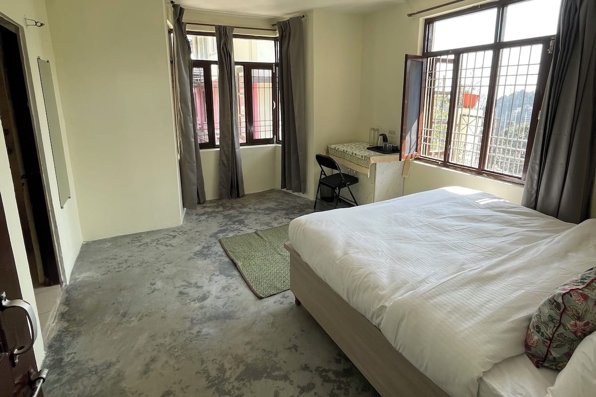 Een hotelkamer met een groot bed, een bureau en uitzicht door de ramen.