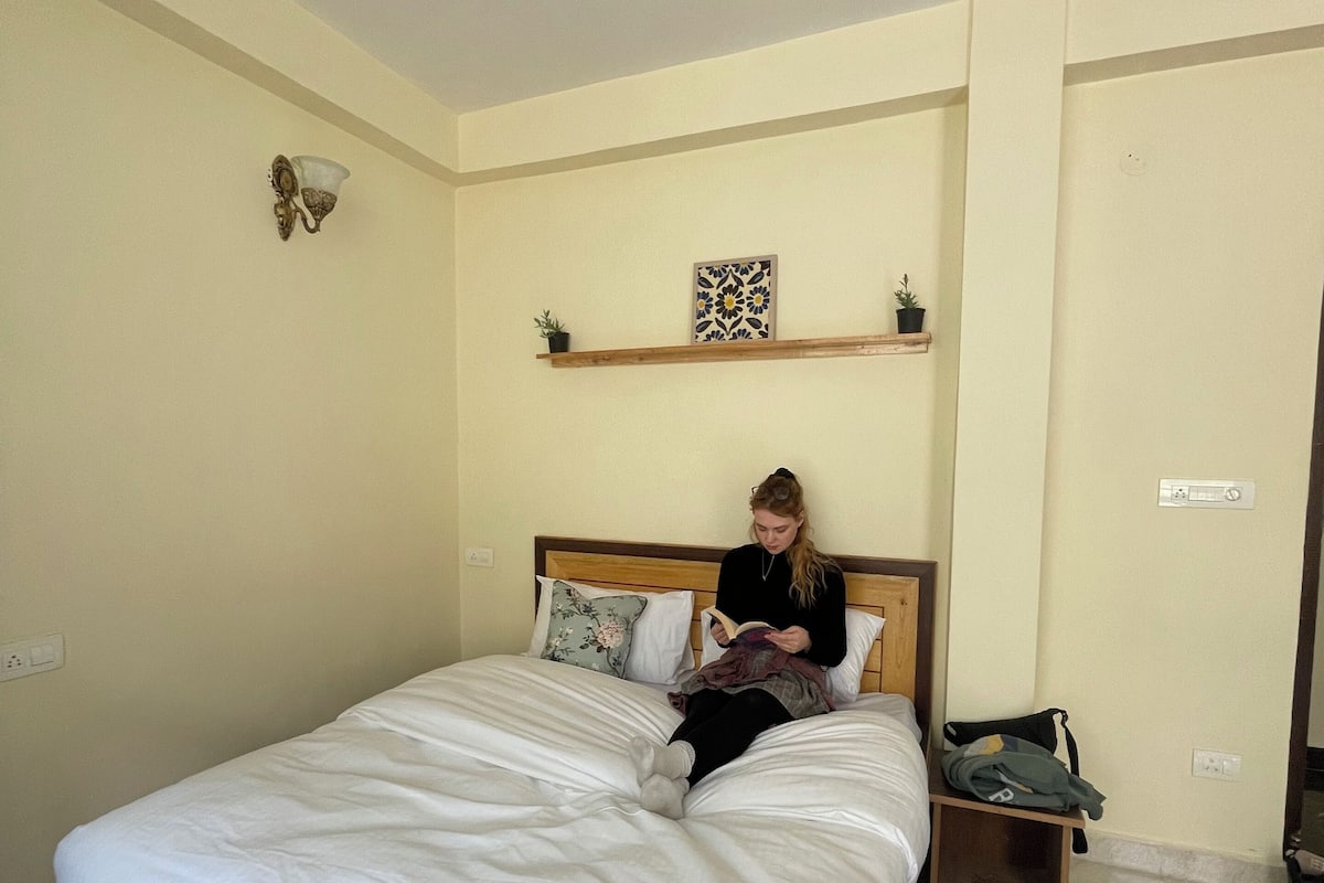 Een slaapkamer met een groot bed, een nachtkastje, een plafondventilator en een plank met decoratieve objecten.