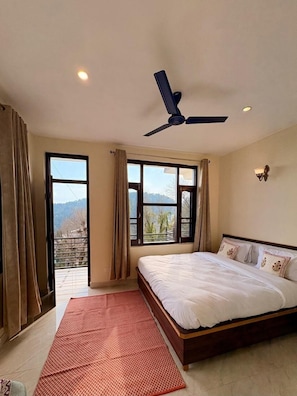 Un dormitorio con cama, ventilador de techo, ventanas amplias y vistas al exterior.