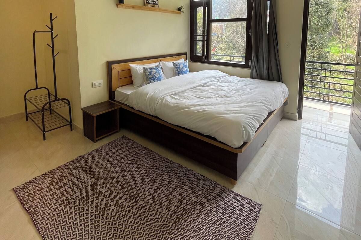Een slaapkamer met een bed, een plafondventilator, een raam met gordijnen en uitzicht op groen.