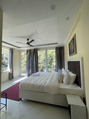 Habitación de hotel con una cama grande, ventilador de techo y ventanas con cortinas.