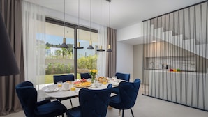 Un espace repas moderne avec une grande table, des chaises bleues et une vue sur l’extérieur.
