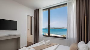 Une chambre d’hôtel avec un lit, un bureau, une télévision et une grande fenêtre donnant sur la mer.
