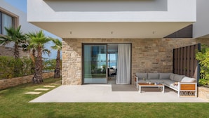 Une maison moderne avec une façade en pierre, une porte vitrée donnant sur un patio et un espace salon comprenant un canapé et une table basse.