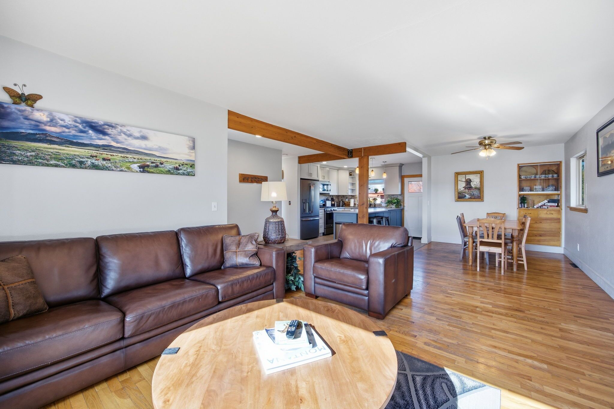 A modern living room with a brown leather sofa, a wooden coffee table, and a dining area with a wooden table and chairs.