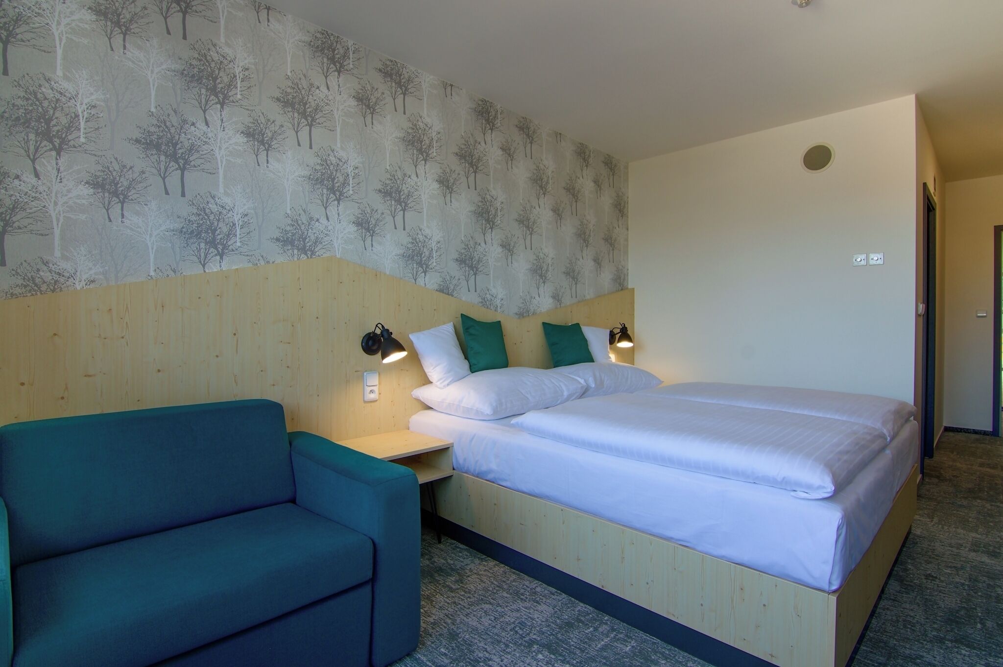 Een hotelkamer met een bed, een blauwe bank en een muur met een boommotief.