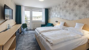 Ein Hotelzimmer mit zwei Betten, einem Schreibtisch, einem Stuhl, einem Fernseher und einem Fenster mit Vorhängen.