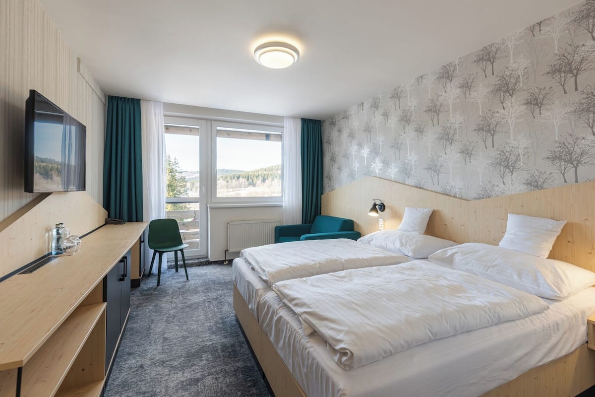 Une chambre d’hôtel avec deux lits, un bureau, une chaise, une télévision et une fenêtre avec des rideaux.