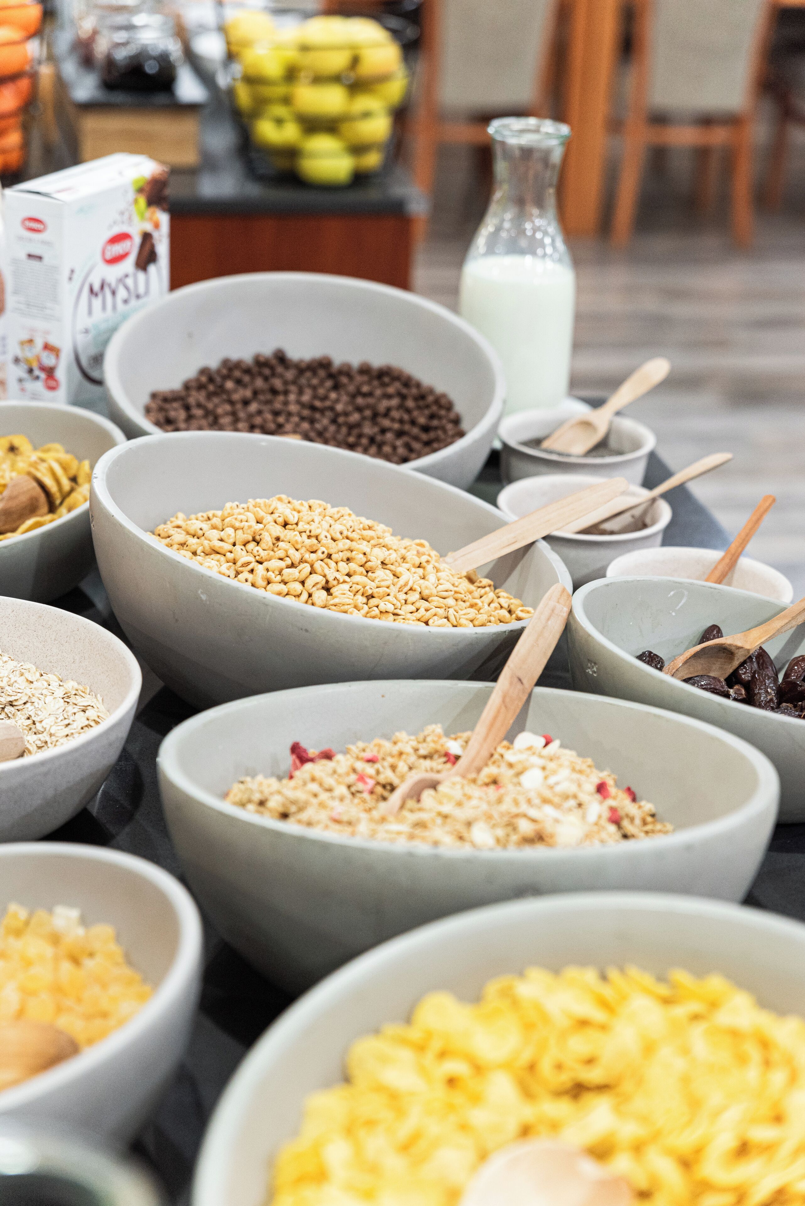 Diversos alimentos en recipientes sobre una mesa, como cereales, frutos secos y frutas deshidratadas.