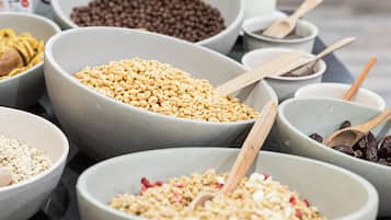 Diversos alimentos en recipientes sobre una mesa, como cereales, frutos secos y frutas deshidratadas.